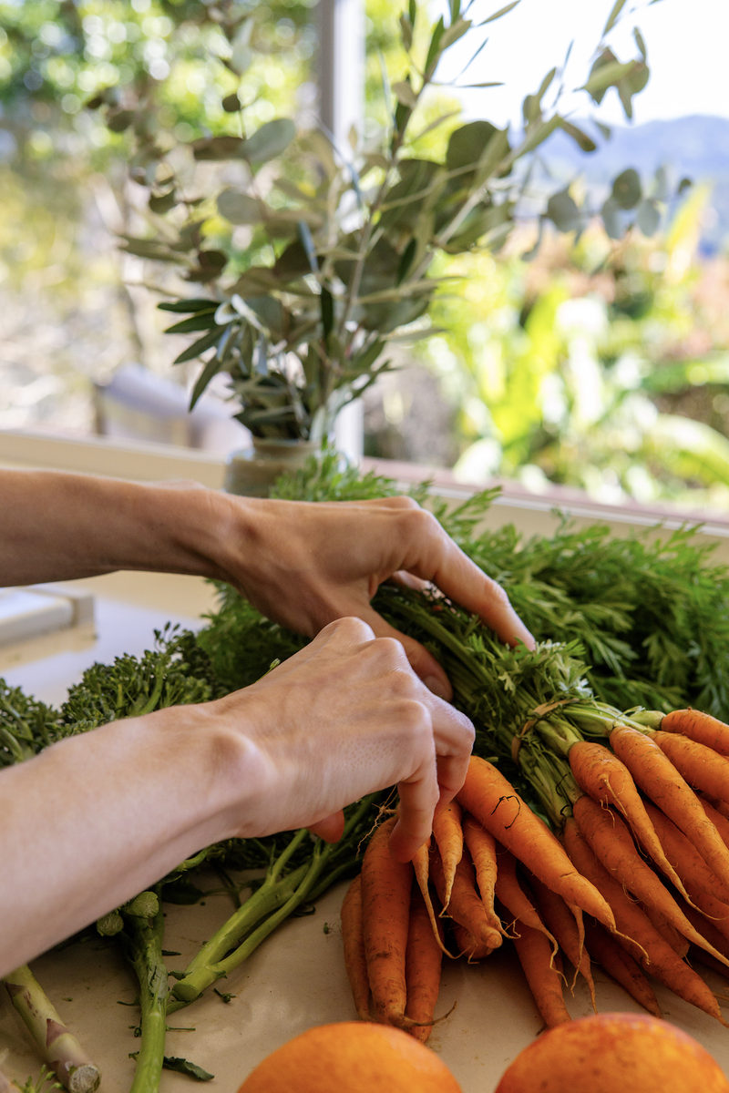 Fresh carrots and greens being prepared at the kitchen bench