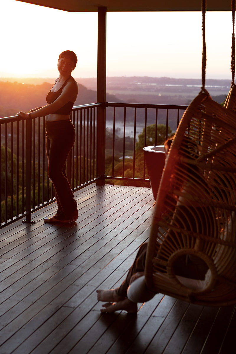 Guest standing at the deck rail at sunset beside a hanging chair