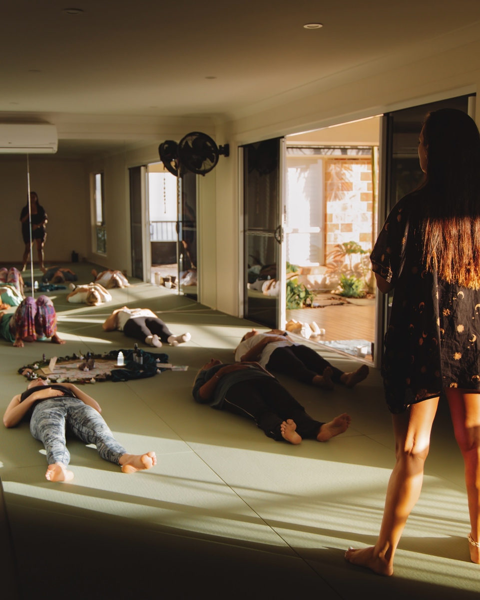 A facilitator guiding a group resting on mats in the studio