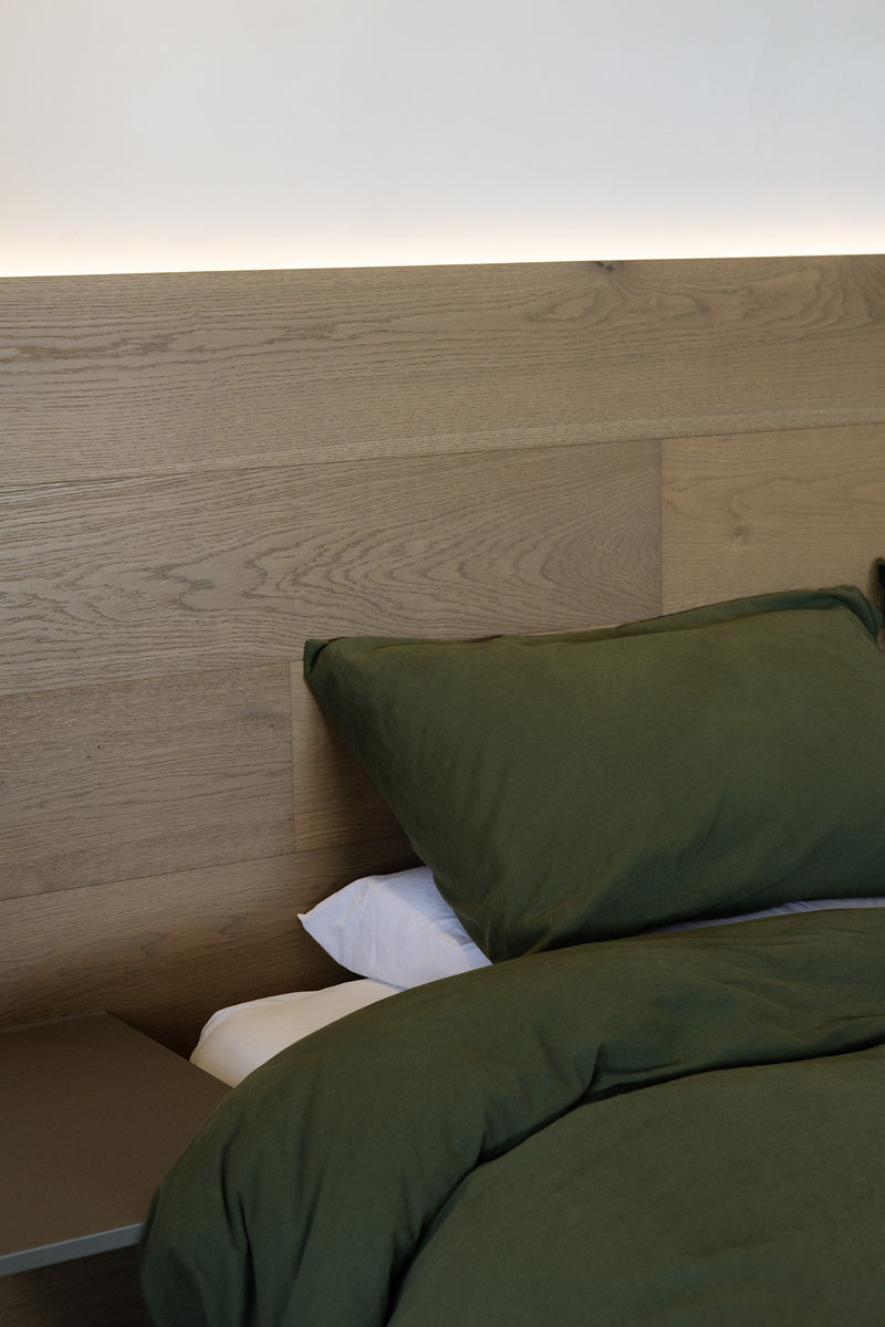 Bed made with green linen beneath a timber bedhead