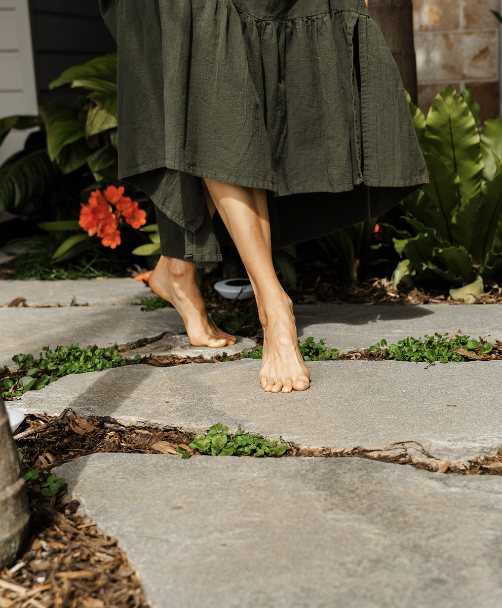 Bare feet on the stone garden path between ferns and clivias